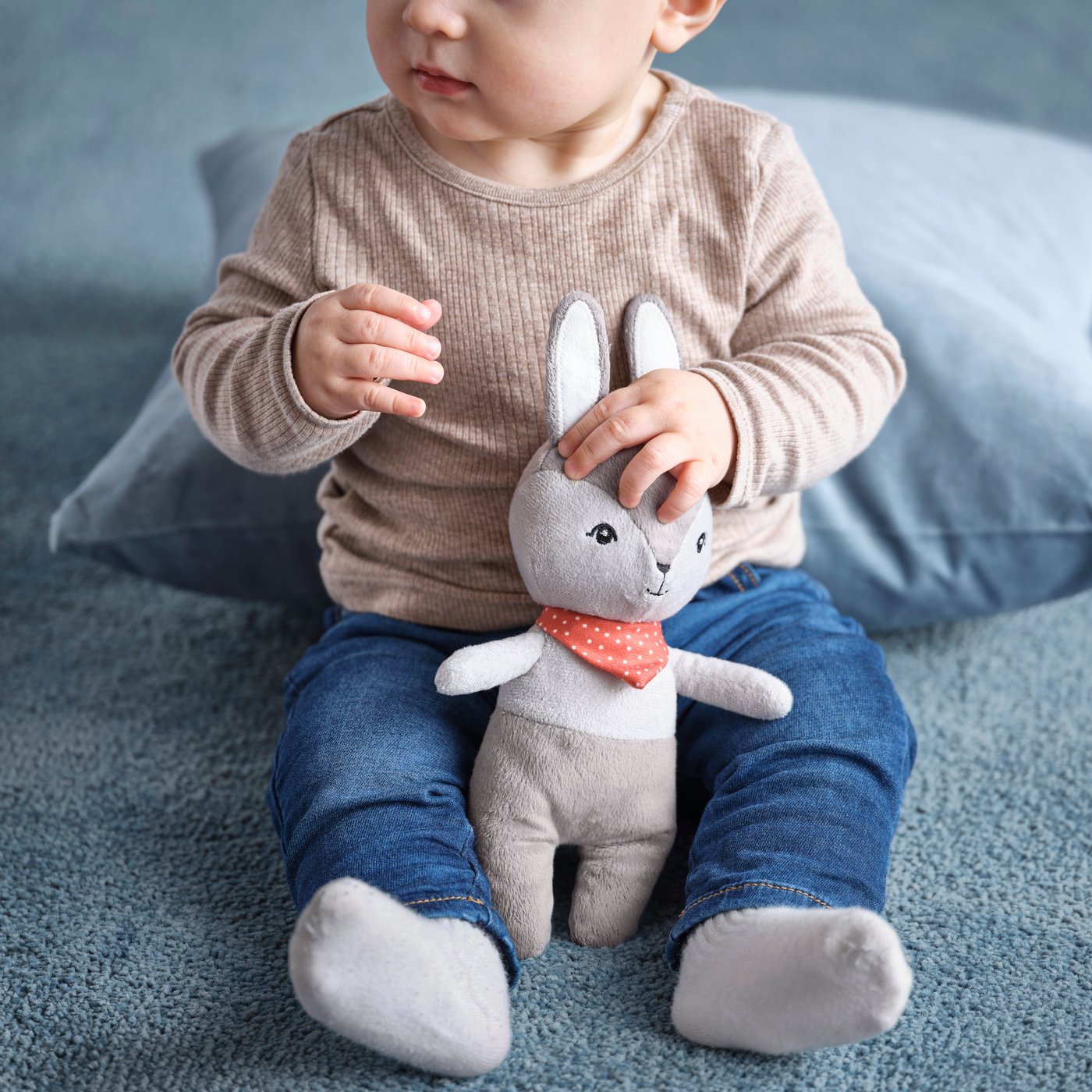 Baby holding a grey GULLIGAST bunny soft toy.