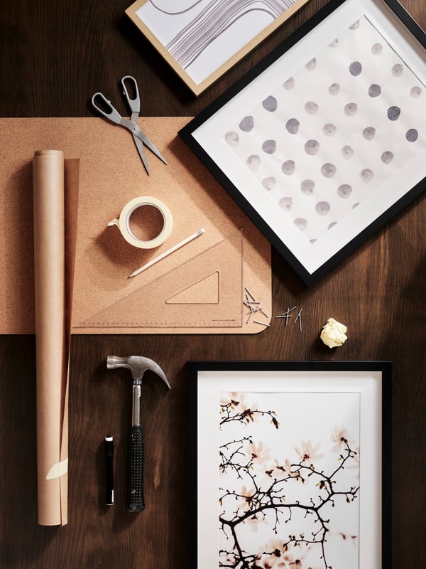 Scattered items on a dark-wood surface, including SVÄRDFISK scissors, a SUSIG cork desk pad, a paper roll and RÖDALM frames.