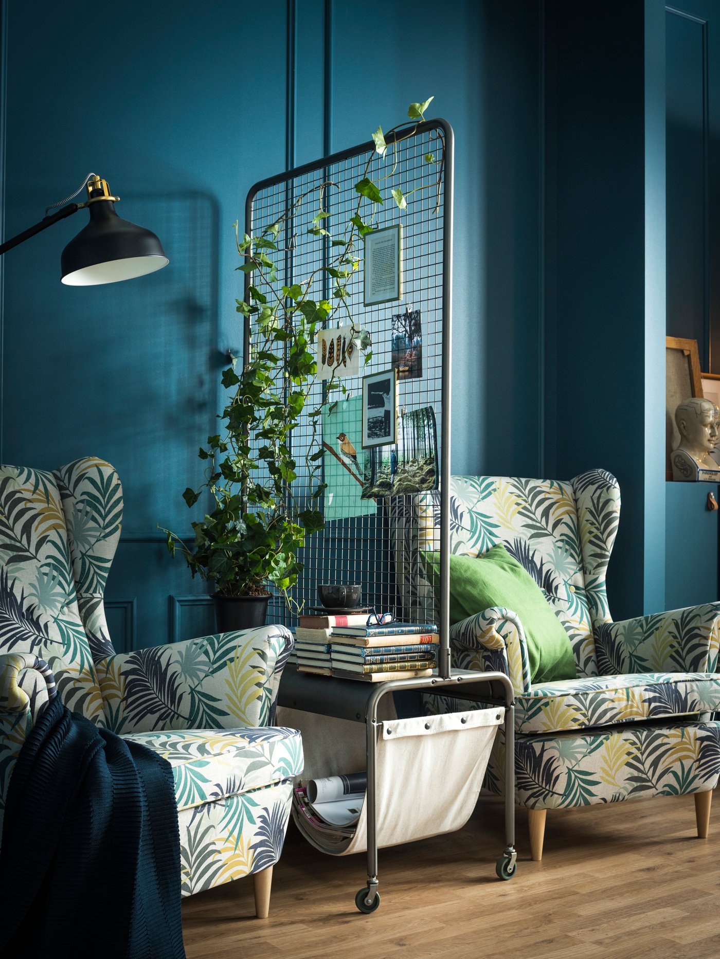 Two armchairs separated by a room divider holding a plant, magazine and book storage.