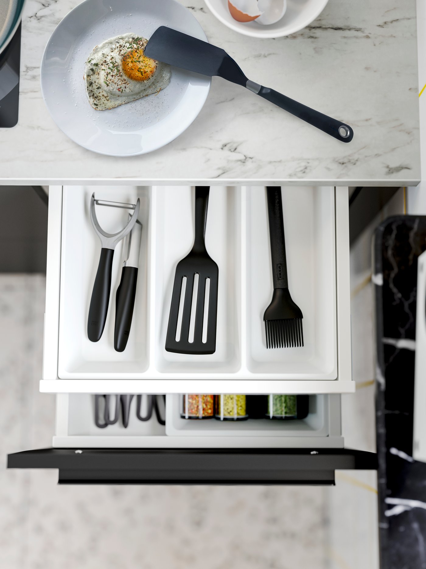 Geöffnete Küchenschublade mit praktischen Küchenhelfern wie Pfannenwender, Sparschäler und Gewürzaufbewahrung.