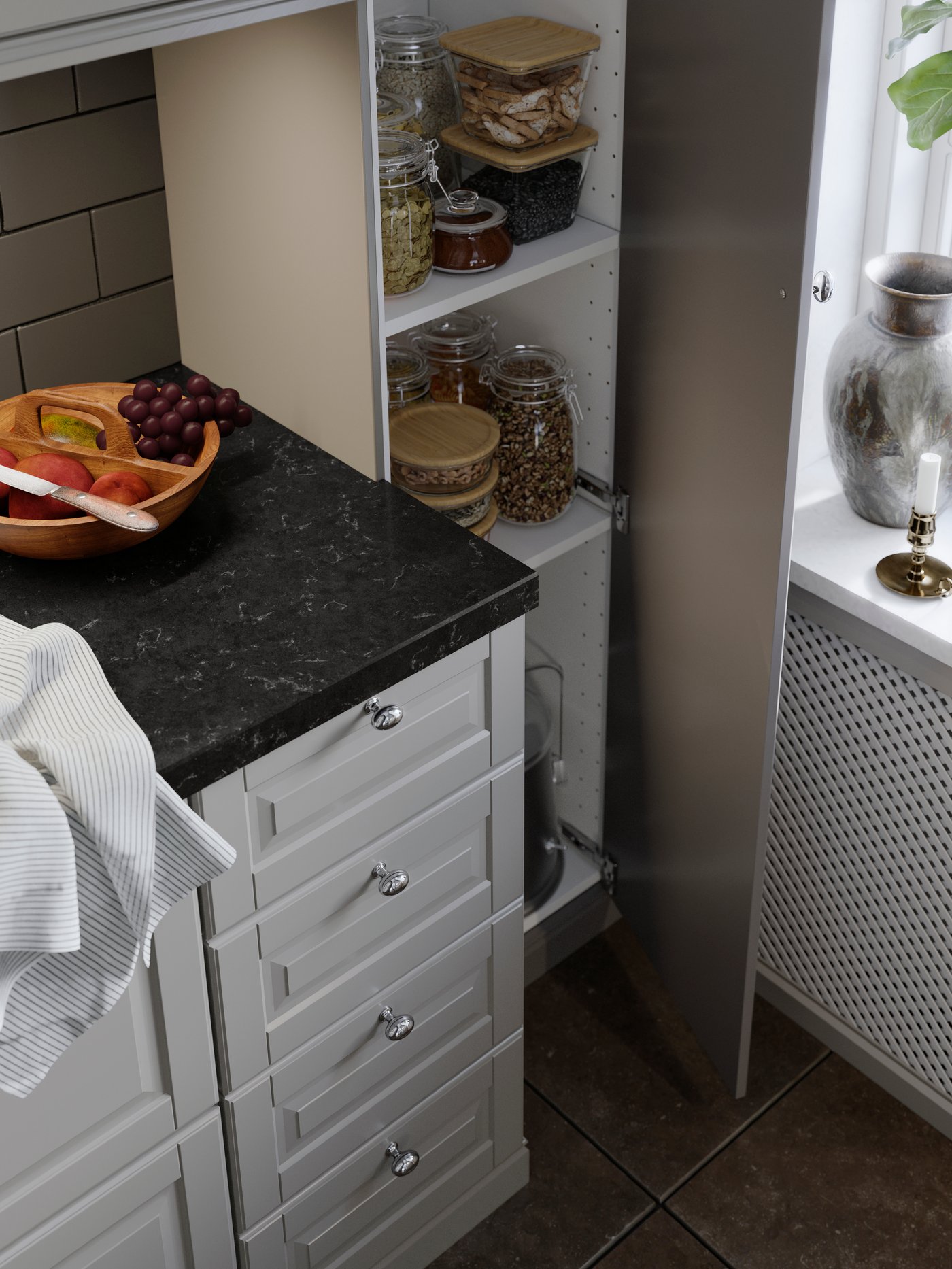Ett kök med vit skåpinredning och svart bänkskiva. En öppen hög skåpsdörr visar hyllor med glasburkar fyllda med matvaror. På bänken står en fruktskål och en kökshandduk.