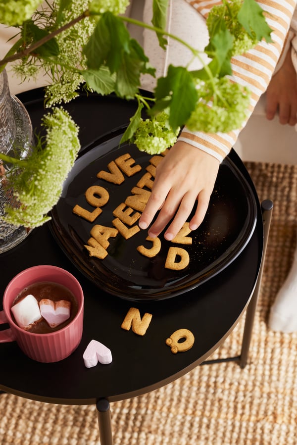 En person stavar ut order "love" på ett sidobord med bokstavsformade KAFFEREP-kakor.