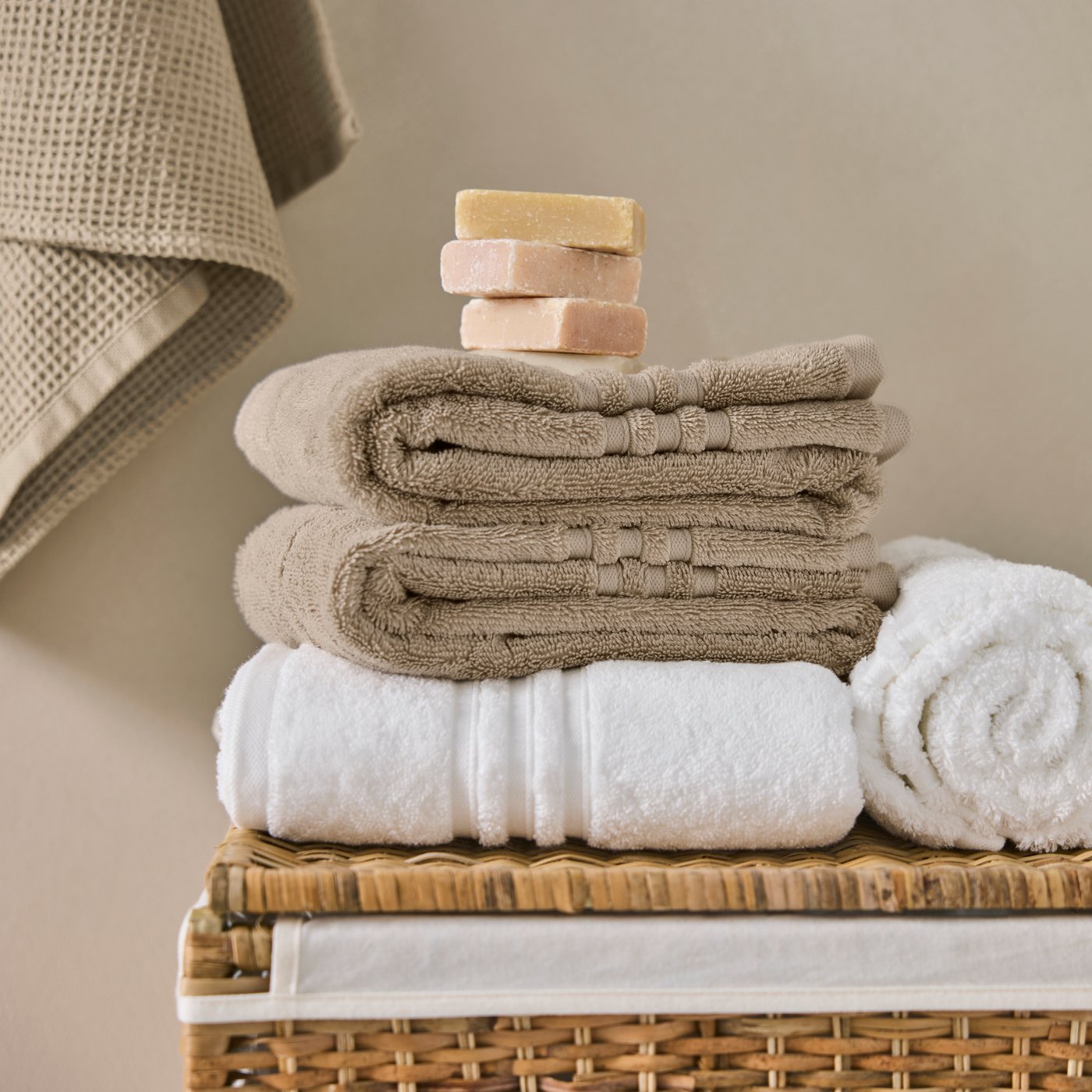 A bathroom scene with neatly stacked towels includes a beige BROKGLIM bath towel on a wicker basket next to a white towel.