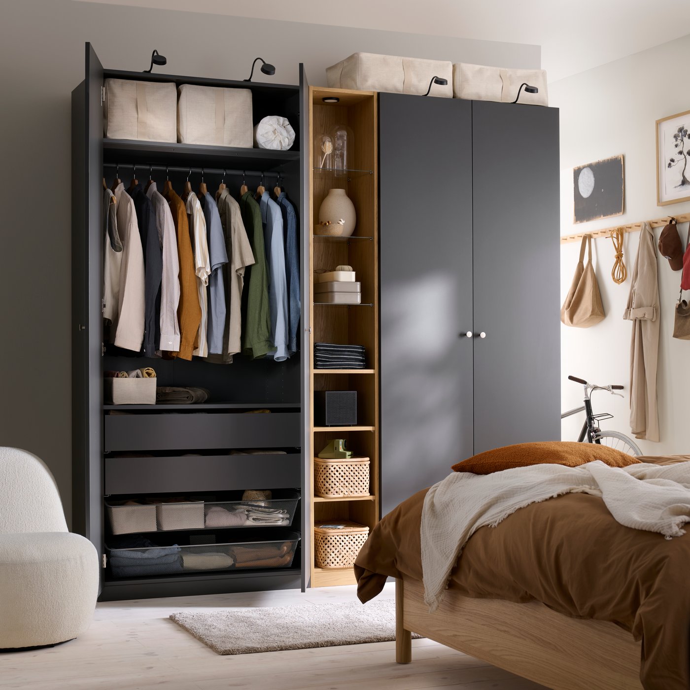 A bedroom with an open PAX wardrobe featuring dark grey FORSAND doors with clothes hanging inside and shelves.
