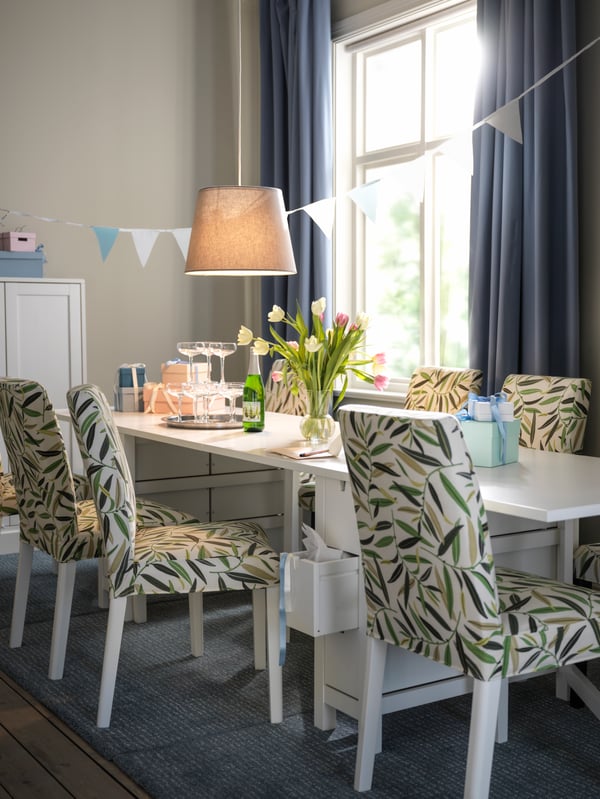 A festively set dinner area with a white NORDEN gateleg table, white-and-multicolour BERGMUND chairs, and decorations.