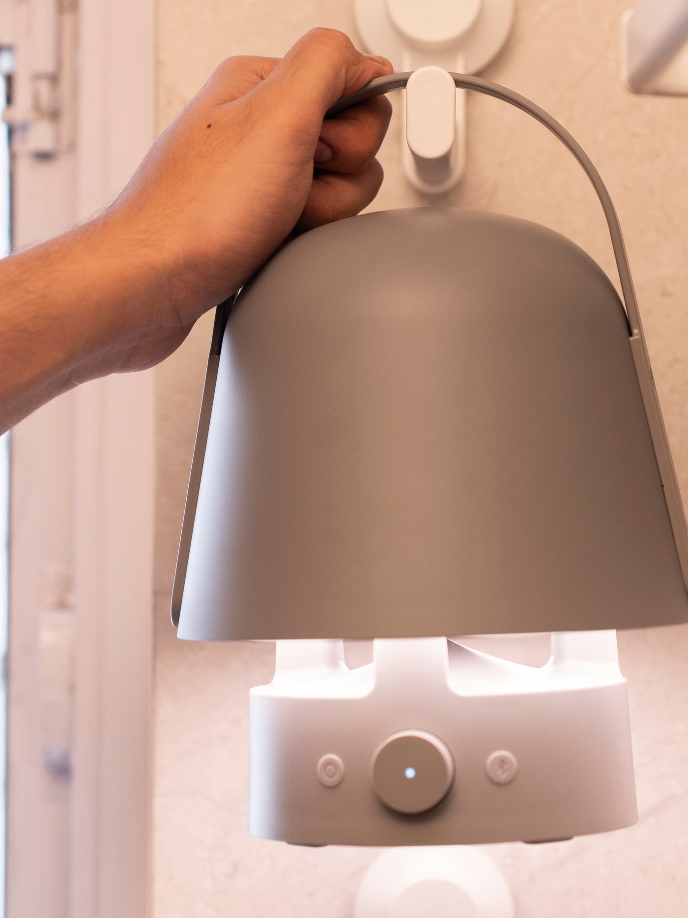 A hand hangs up a VAPPEBY bluetooth speaker lamp on a TISKEN hook on the bathroom wall.