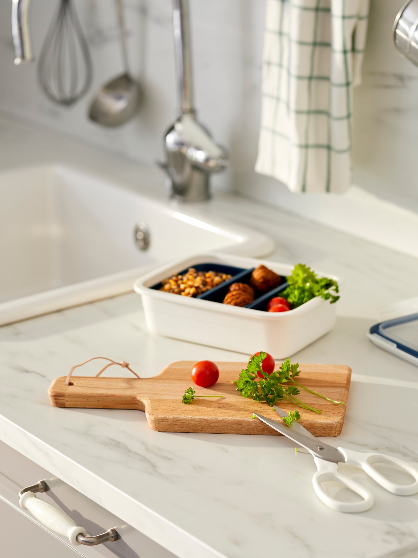 Küchenarbeitsplatte mit einer Lunchbox, einem Schneidebrett, Tomaten und ein paar Kräutern