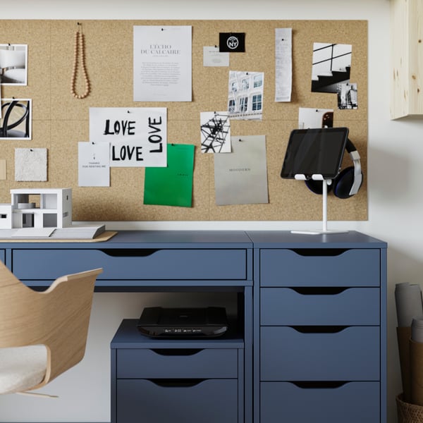 An ALEX desk and two drawer units on castors in black-blue, with a cork memo board above and a conference chair in front.