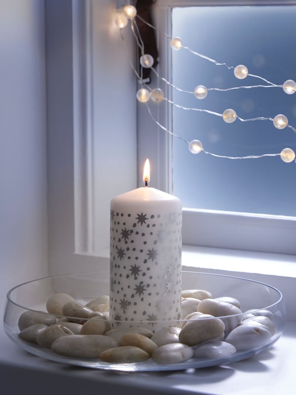 Eine LED-Lichterkette aus unserer STRÅLA Serie und eine weihnachtliche Kerze auf der Fensterbank.