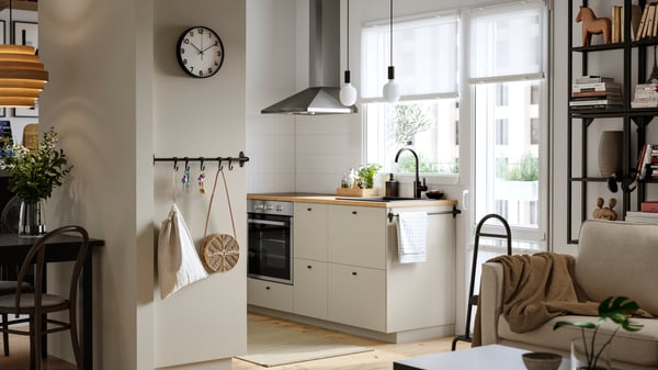 A kitchen with a window and a balcony door has beige HAVSTORP fronts and a RYTMISK wall mounted extractor hood.