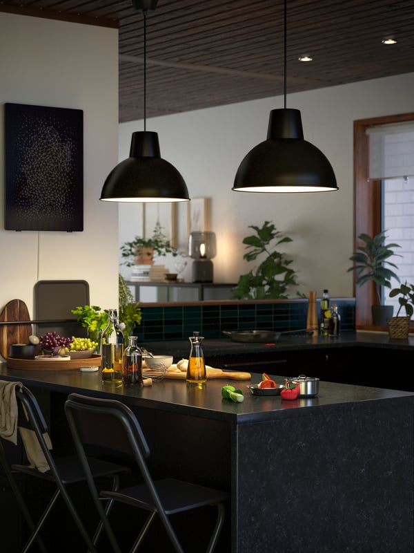 Two black SKURUP hanging pendant lamps are lighting up a kitchen island with a KASKER worktop in anthracite stone effect. 