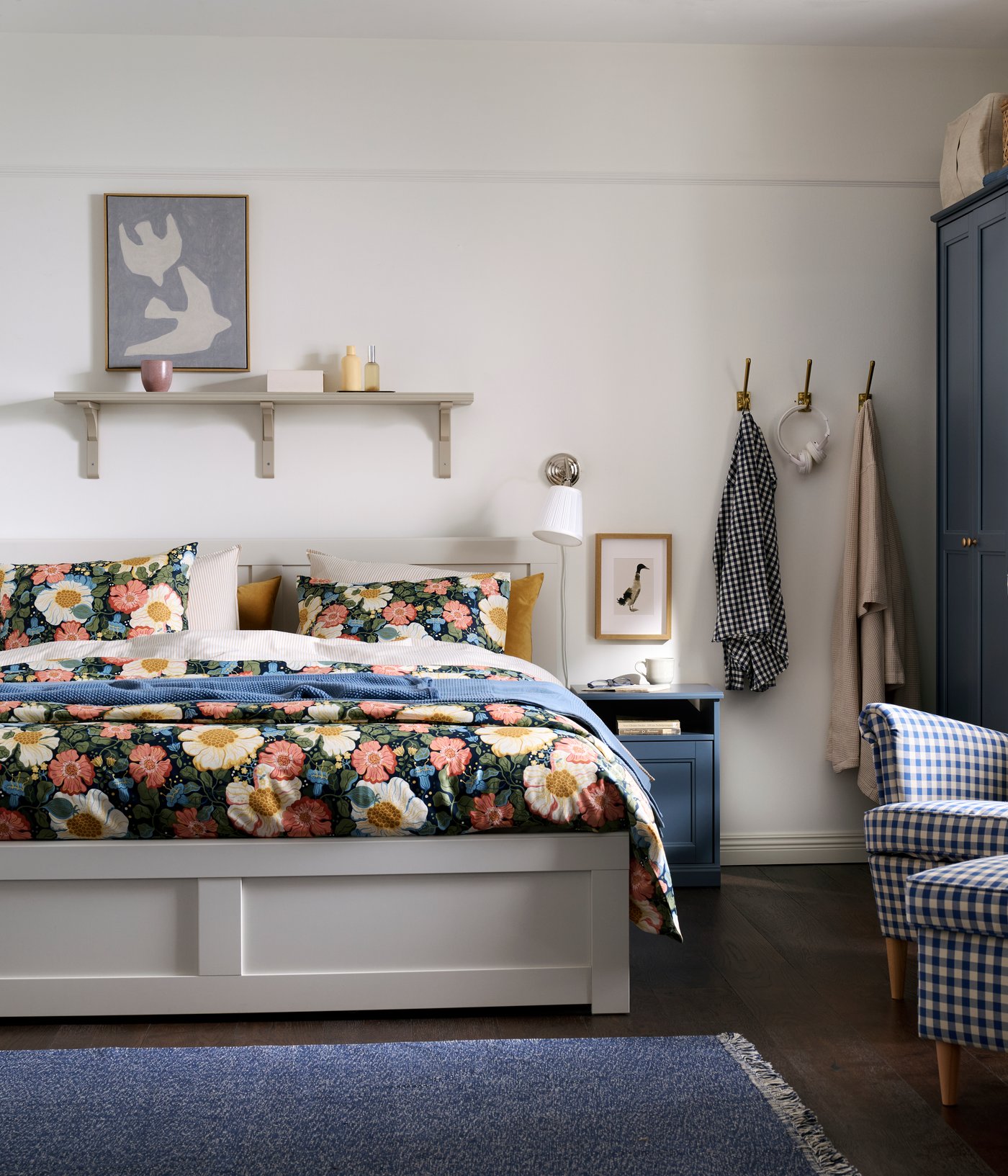 A traditional-style bedroom with a white FÅGELFJÄLLET bed, a blue FÅGELFJÄLLET bedside table and wardrobe, and floral bedding.