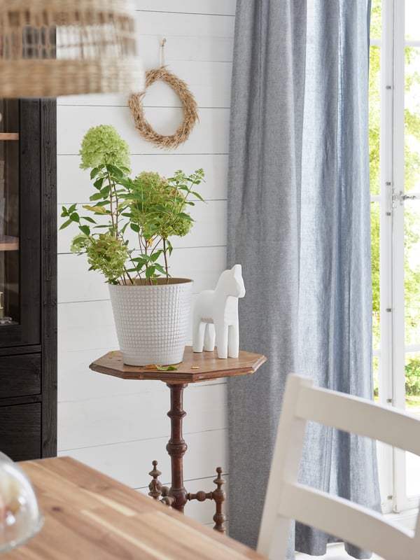 Un cache-pot CHIAFRÖN avec des plantes vertes près d’une décoration blanche en forme de cheval sur une table d’appoint de style rétro.