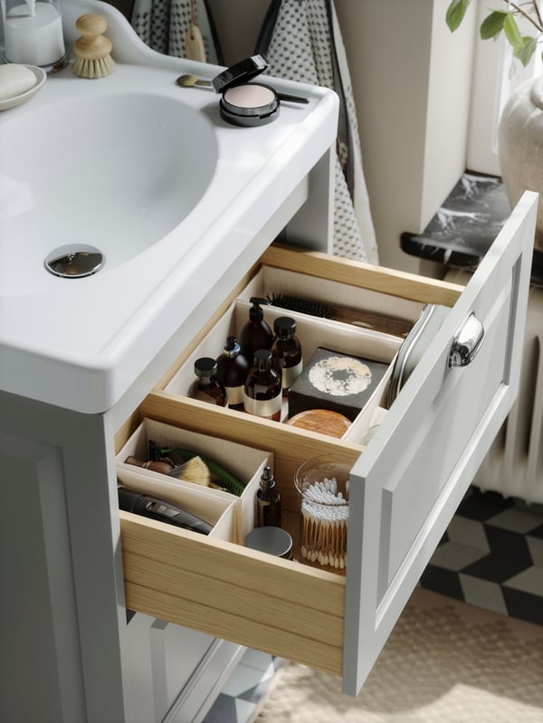 A deep bathroom drawer in light grey, neatly organised with BOLLÖSUND boxes inside filled with bottles and cotton pads.
