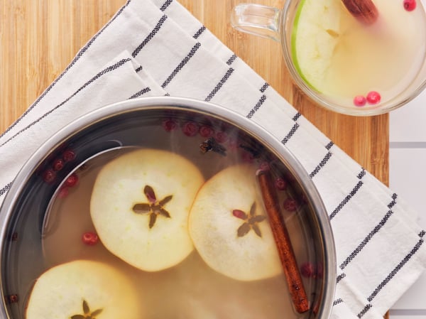 A pot of warm FLÖJT green tea with apple slices and spices on a striped cloth with a mug on the side.