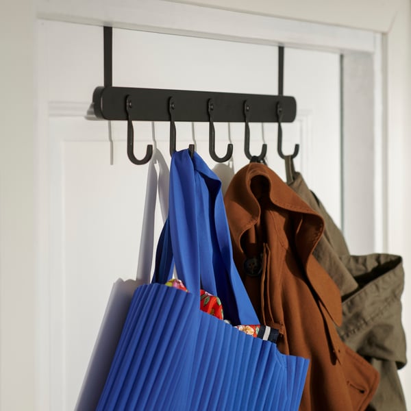 A black ÅRSJÖN hanger on the back of a white door with coats and scarves hanging on it.