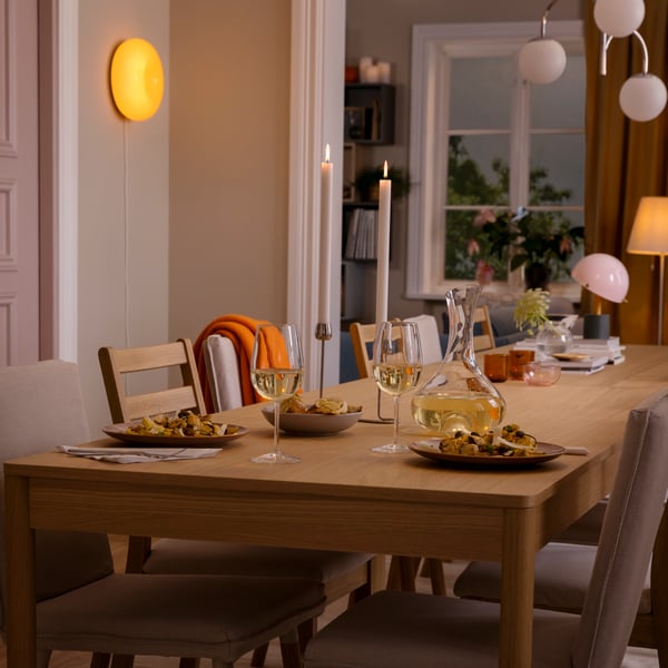 A TONSTAD table in oak veneer, set for a festive occasion with STORSINT glasses, a STORSINT carafe and FÄRGKLAR tableware.