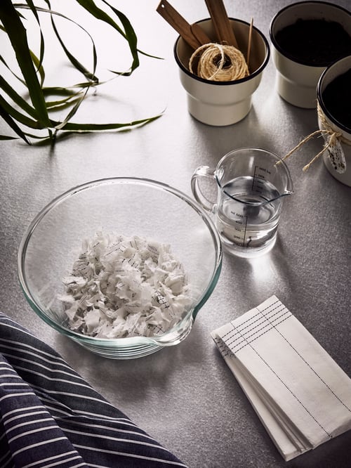 A VARDAGEN bowl in clear glass with shredded paper napkins, next to a measuring jug and white plant pots.