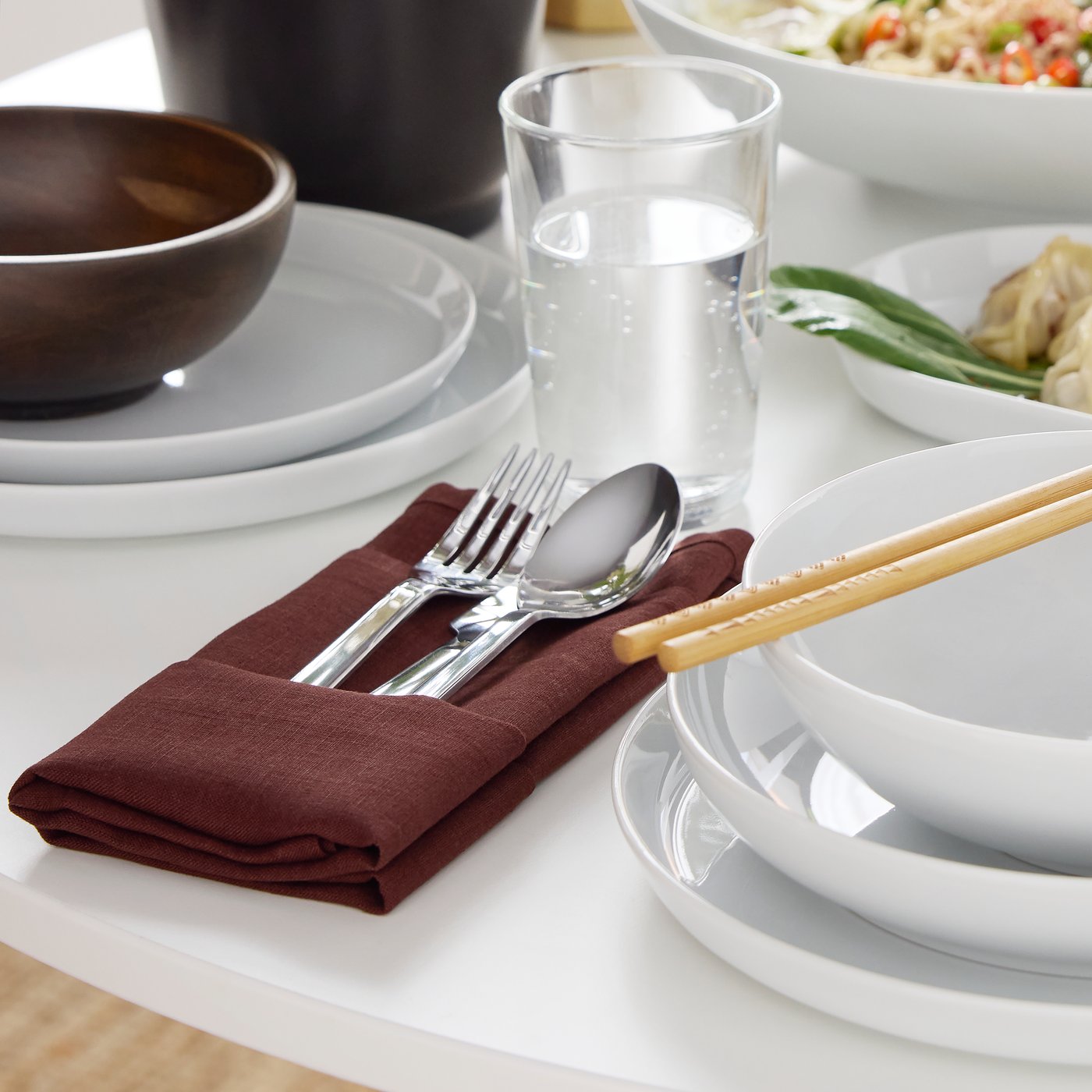 A fork, a knife and a spoon from the IKEA 365+ cutlery series lie on a folded dark red STOCKHOLM 2025 napkin.