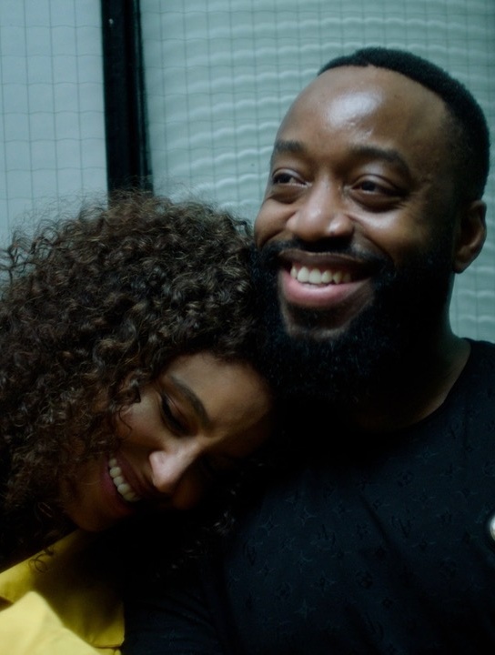 Muzičarka Kanis, glave položene na rame muškarca.