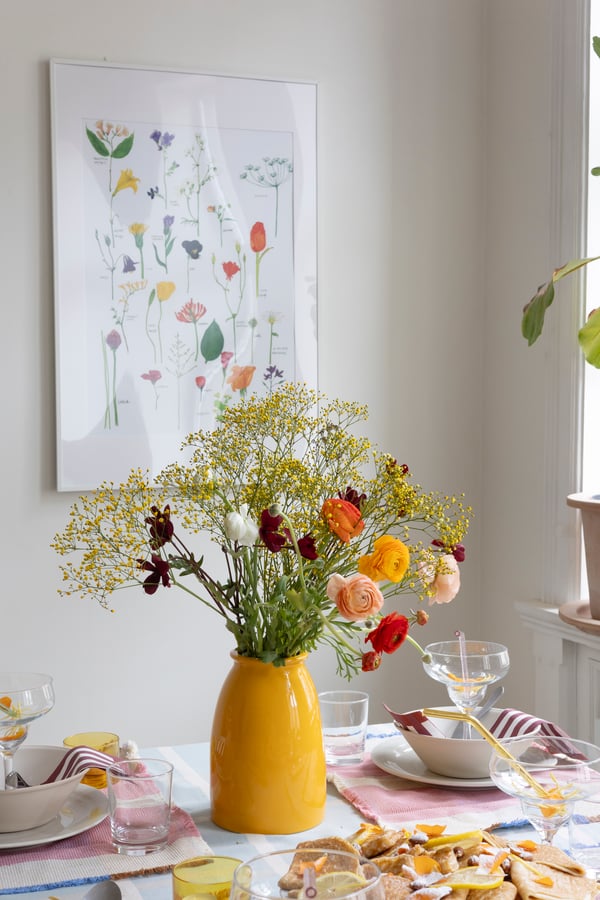 A bright yellow KOPPARBJÖRK vase with an artificial bouquet in it.