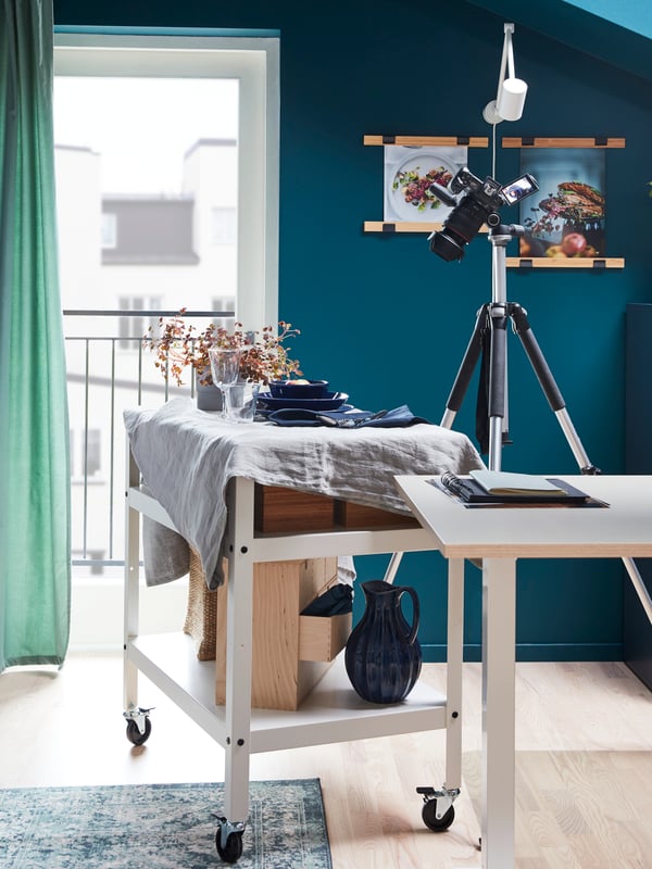 A decorative dinner scene on the top shelf of a trolley with castors, moved next to a camera for a photo shoot.