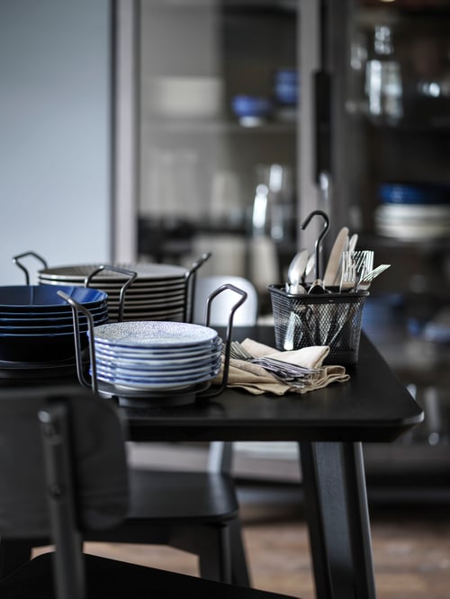 A plate holder with grey plates, a plate holder with white plates, and a cutlery caddy, all set on a black table.