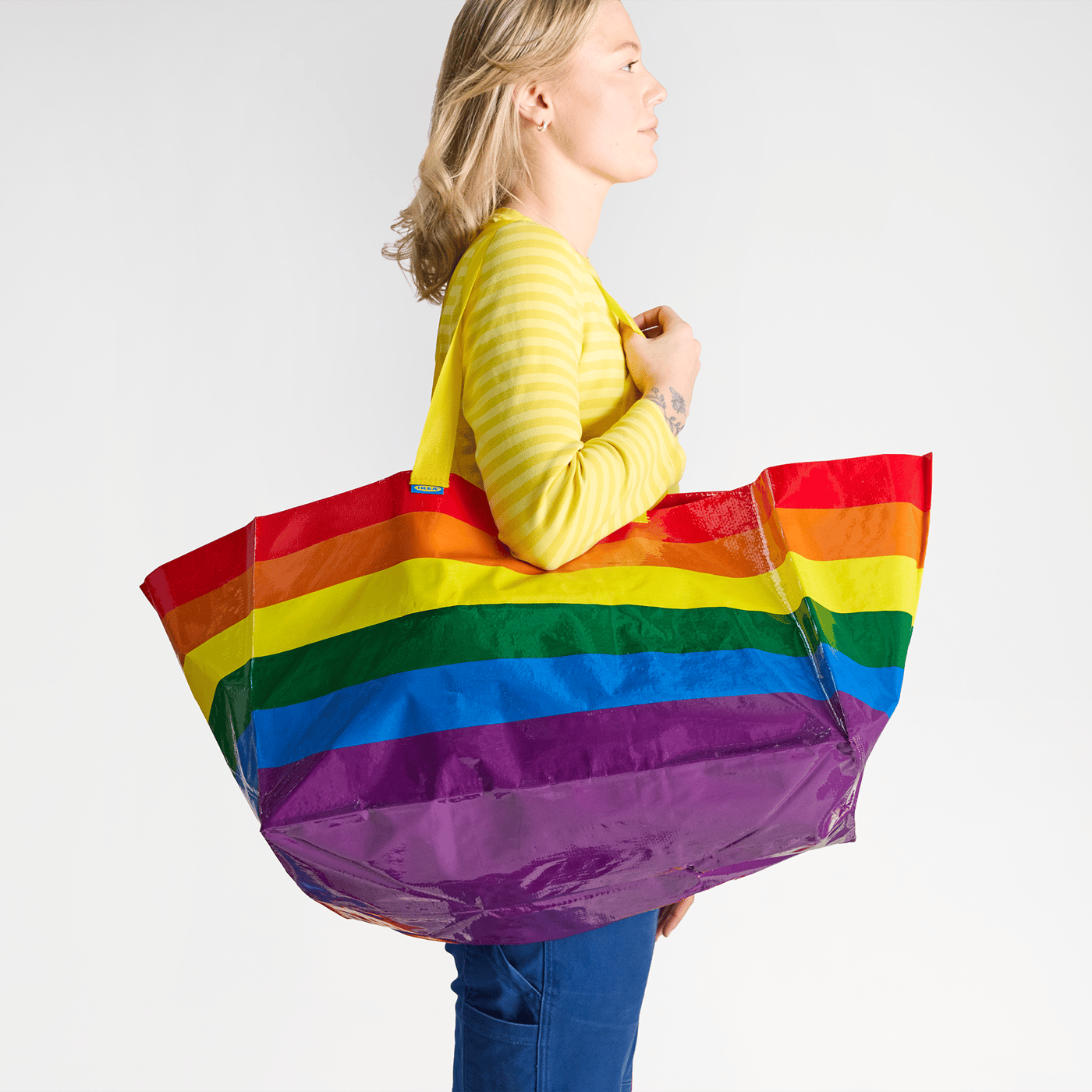 Ein Frau trägt eine Große Tasche über der Schulter, die in Regenbogen-Farben gestreift ist.