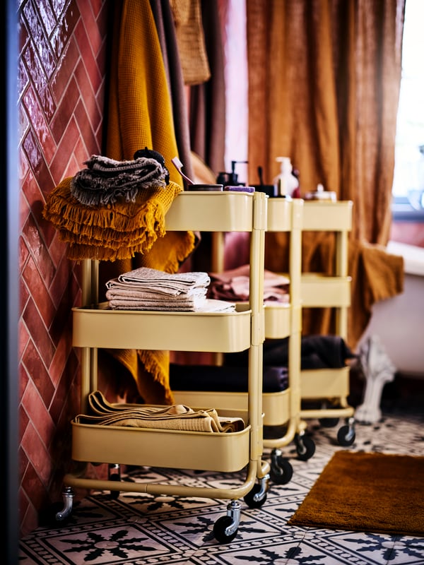 Three mustard yellow RÅSKOG trolleys in a bohemian bathroom.