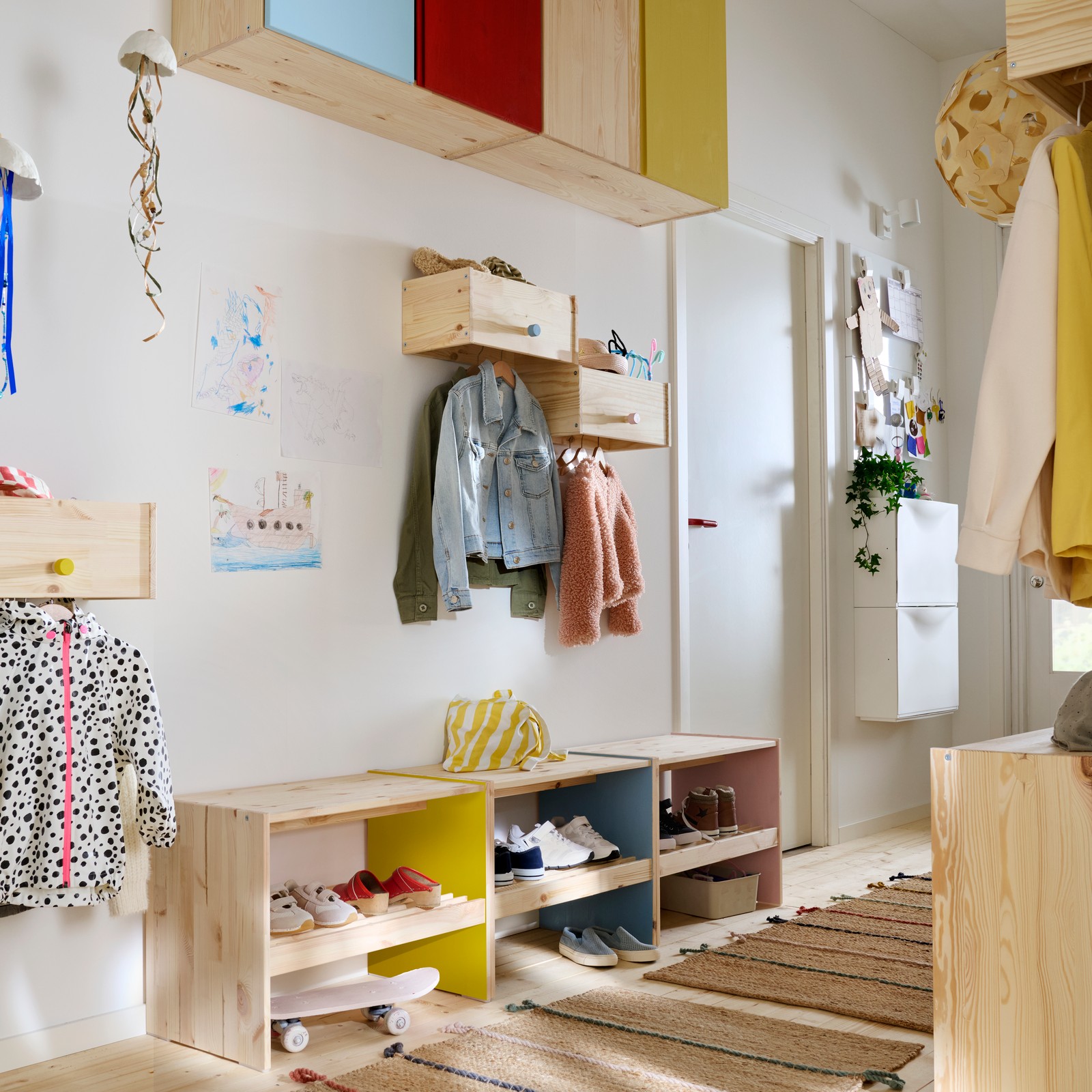 Un hol de familie cu soluții de depozitare RAGGBERG montate la diverse înălțimi, toate din lemn de pin natur, dar cu detalii vopsite în culori vii.