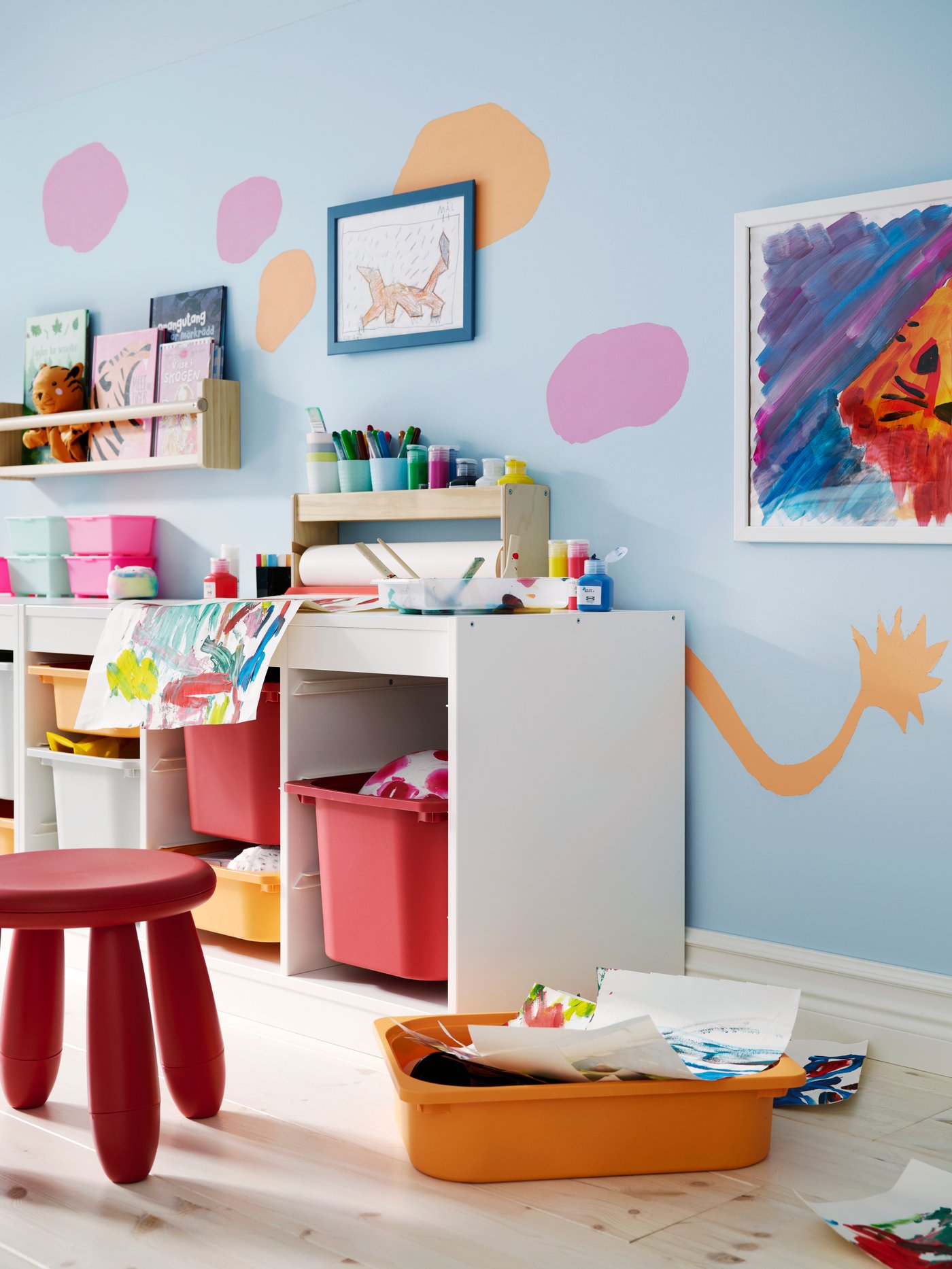 Children’s room with blue walls, and paintings and art supplies all over a TROFAST storage unit with plastic storage boxes.