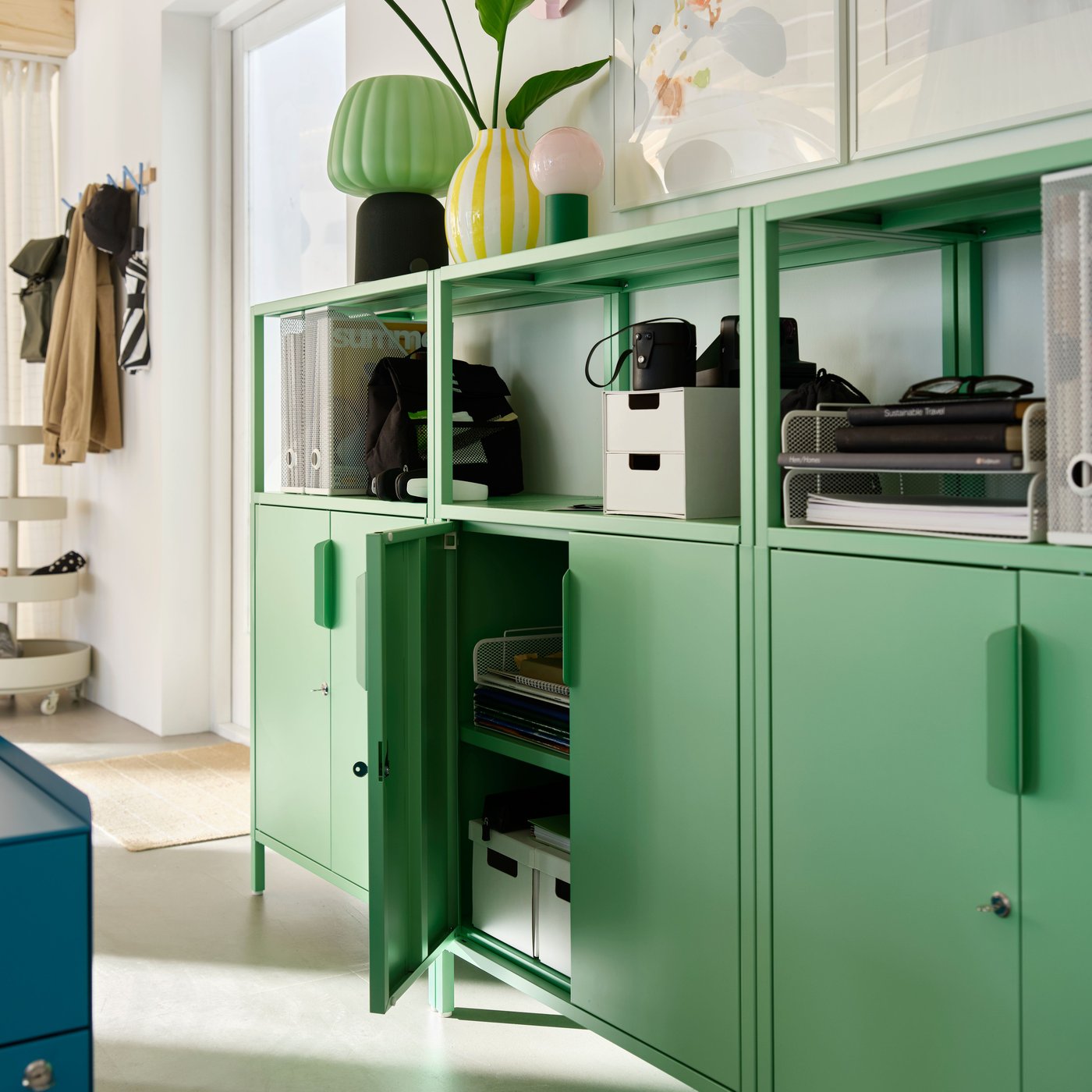 Row of green office cabinets with open shelving above. One cabinet door is open, revealing storage boxes inside.