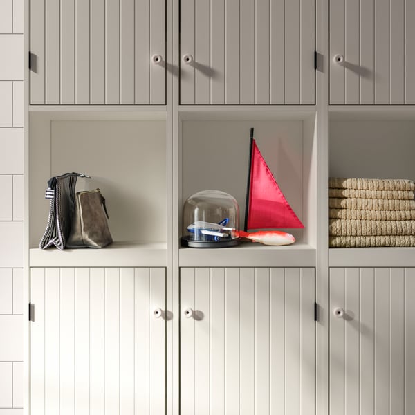 White SILVERÅN bathroom cabinets hold bathroom accessories, a glass jar with object inside and a small boat with a red sail.