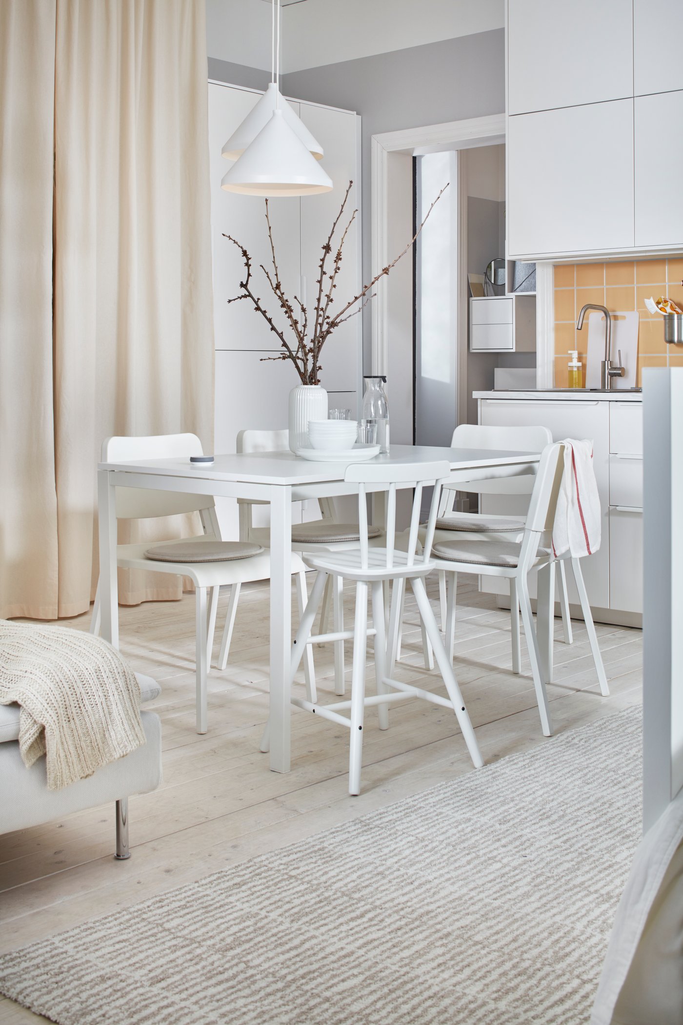 Helle und weiße Einzimmerwohnung mit einem MELLTORP Tisch und TEODORES Stühlen zwischen einer Küche und einem Bett.