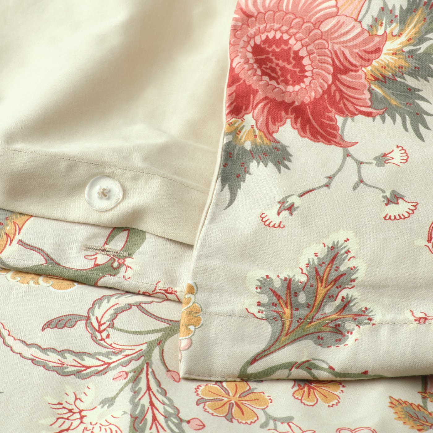 A close up image showing the edges and buttons of light grey beige/mutlicolour NÄSSELKLOCKA bed linen.