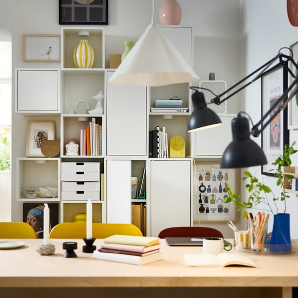 White EKET cabinets are mounted on a white wall behind a BERGSHYTTAN table, and there are things stored on the shelves.