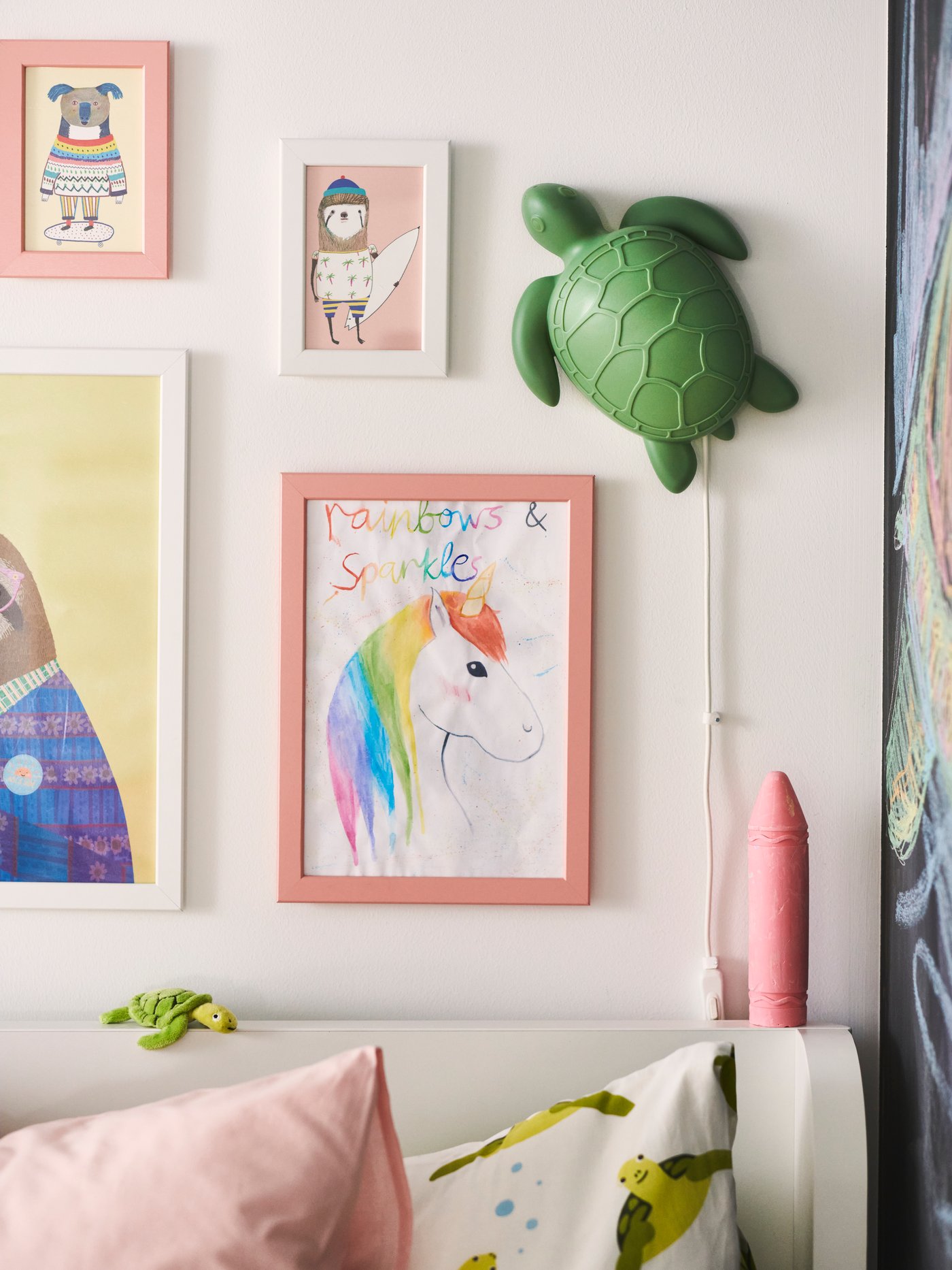 Ci sono cornici di diversi colori e forme e una luce notturna a forma di tartaruga appesa sopra un letto bianco da bambino.