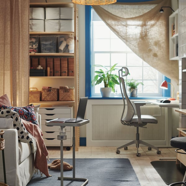 Home office with sofa-bed to the left, work desk at the far right, several bookcases and window in the back.