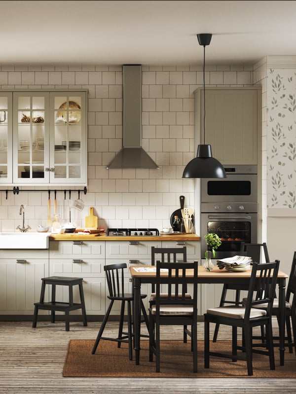 Una cucina in stile countru con ante a vetro STENSUND e cappa in alluminio. Di fronte, un tavolo con sedie nere AGAM e STEFAN.