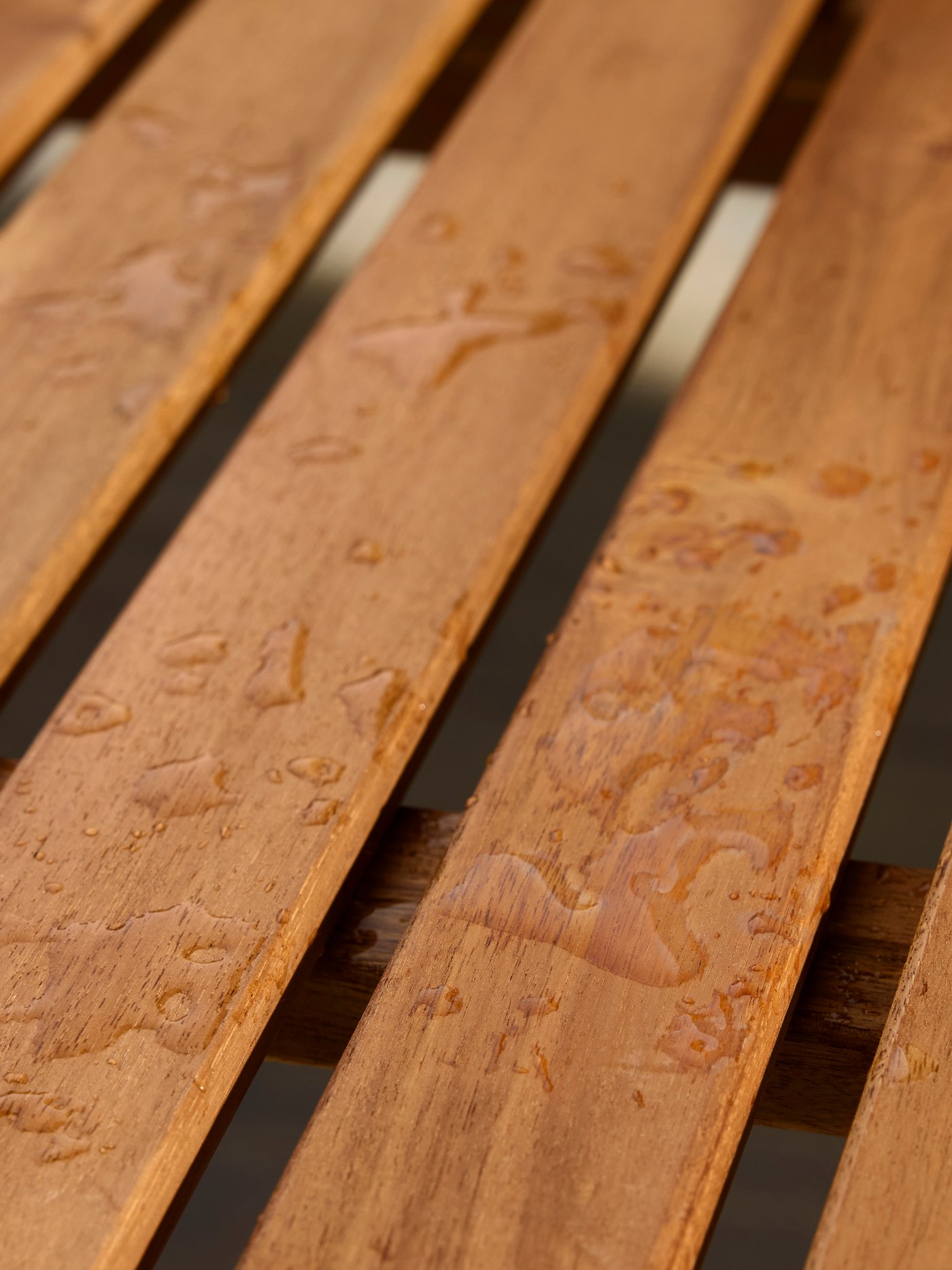 A close-up of a wooden table where raindrops are forming beads on the surface.
