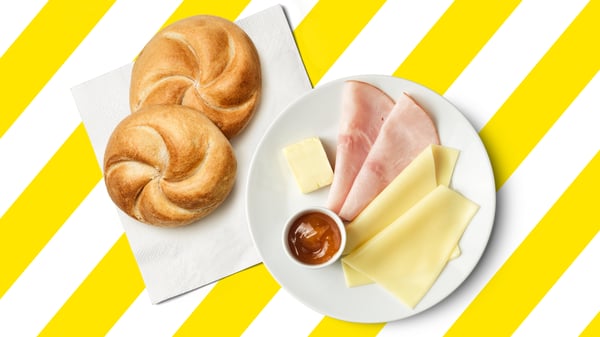 Ein Frühstücksteller mit einer Semmel, Käse, Schinken, Butter und Marmelade.