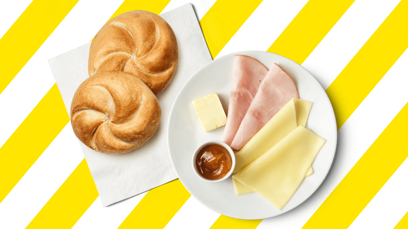 Ein Frühstücksteller mit einer Semmel, Käse, Schinken, Butter und Marmelade.