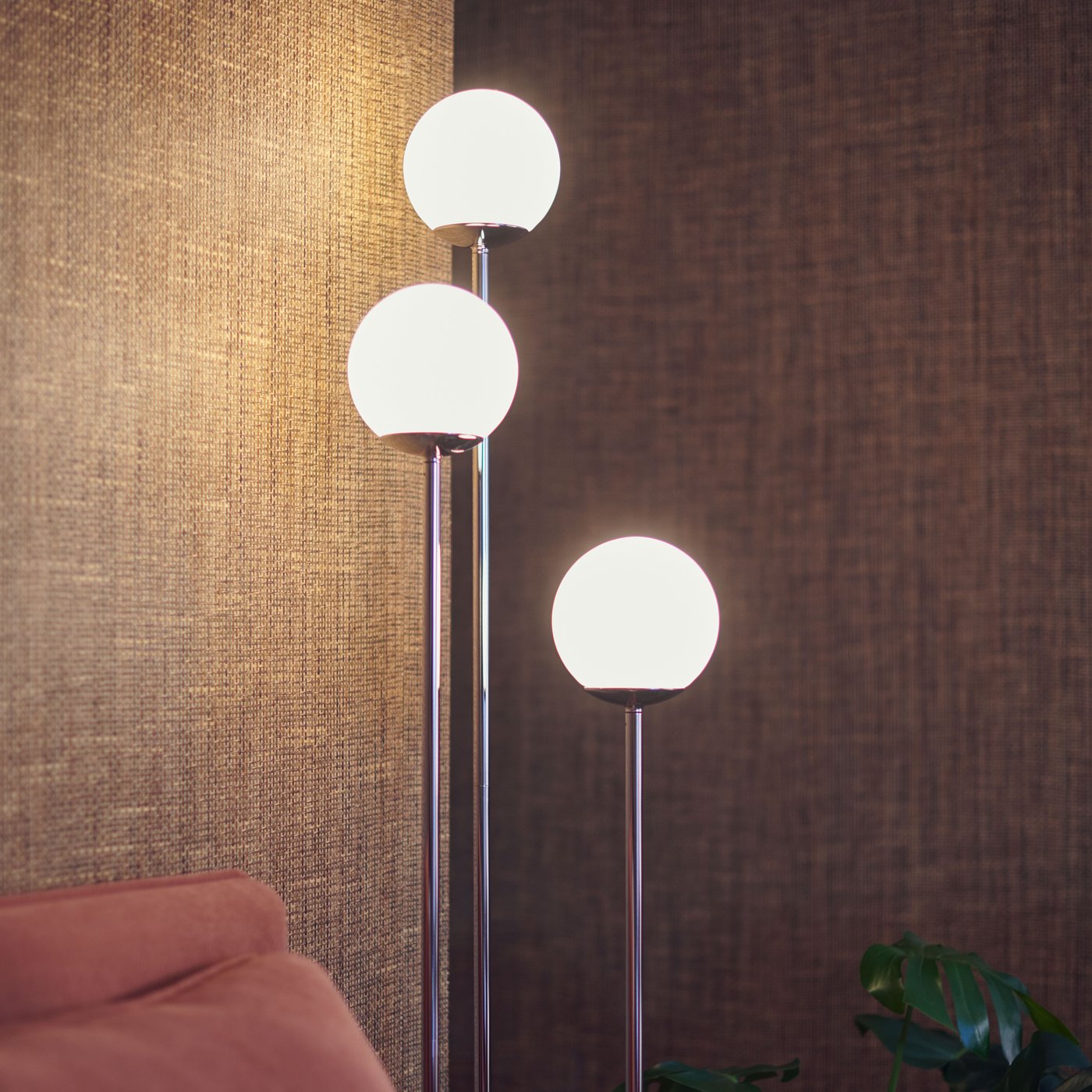A SIMRISHAMN floor lamp with three bulbs giving off a warm glow against natural brown walls in the corner of a living room.