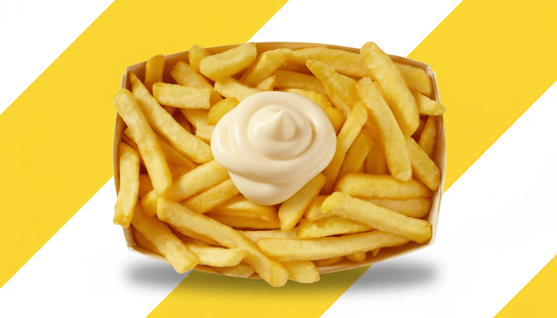 Portie goudgele frieten in een kartonnen bakje, afgewerkt met een royale toef mayonaise, op een achtergrond met gele en witte diagonale strepen.