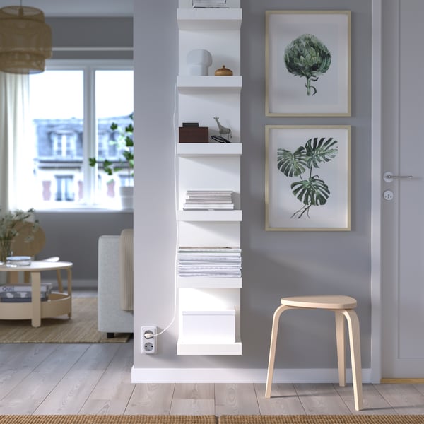 A white LACK wall shelf unit is attached to the wall next to two posters of plants and near a stool.