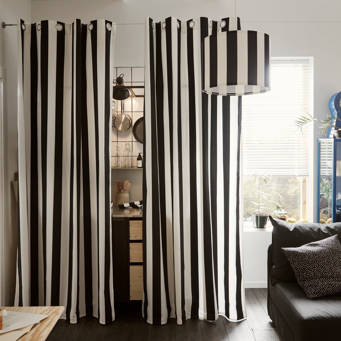 ستائر SLÅNHÖSTMAL مخططة بالأبيض والأسود معلقة حول مطبخ صغير بجوار نافذة طويلة.