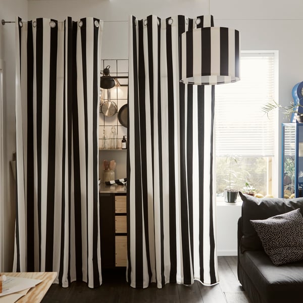The black and white striped SLÅNHÖSTMAL curtains hanging around a kitchenette that is hinted, placed next to a tall window.