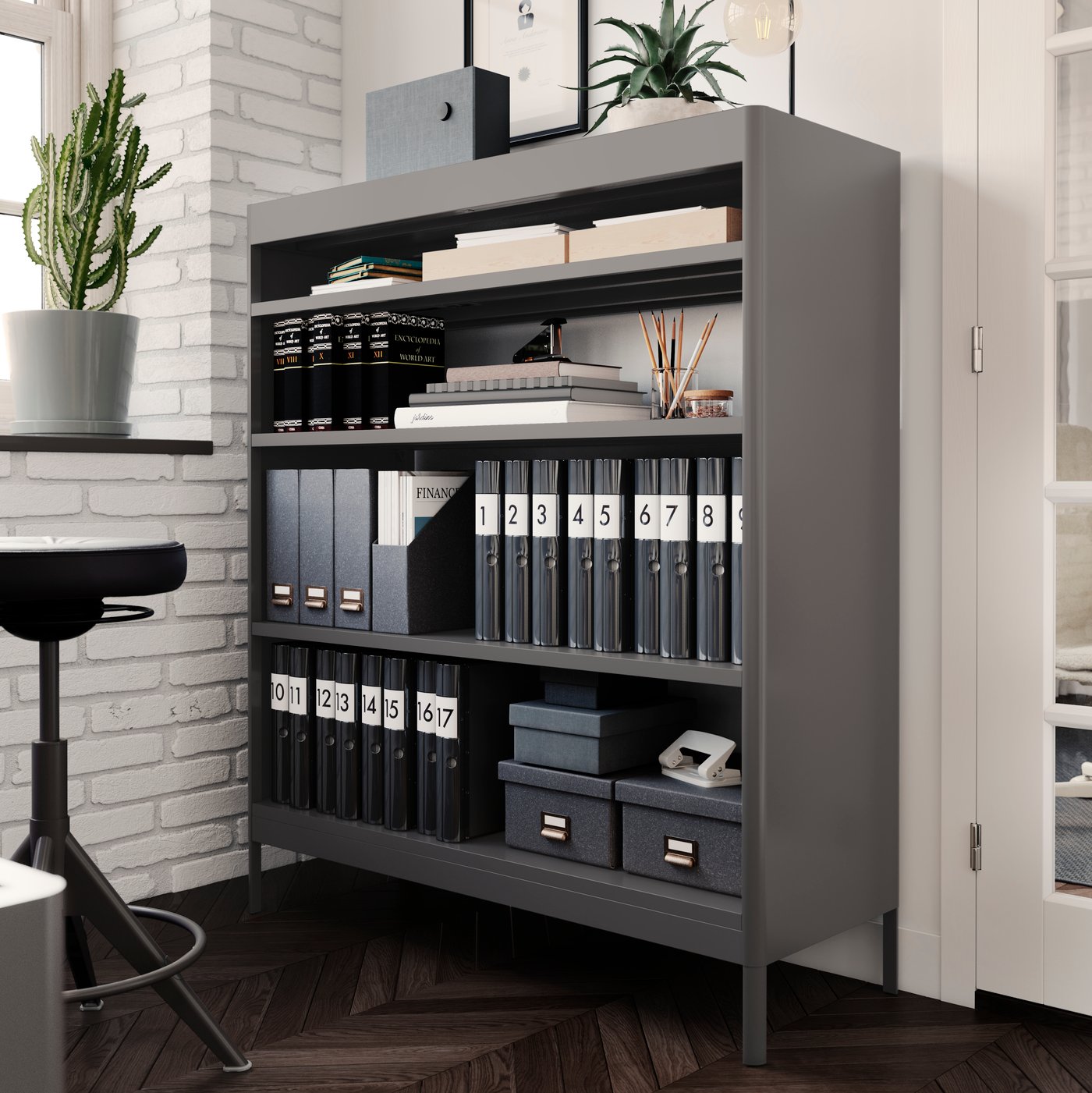A dark grey IDÅSEN shelving unit standing against a white wall with neatly organised magazine files and boxes on its shelves.