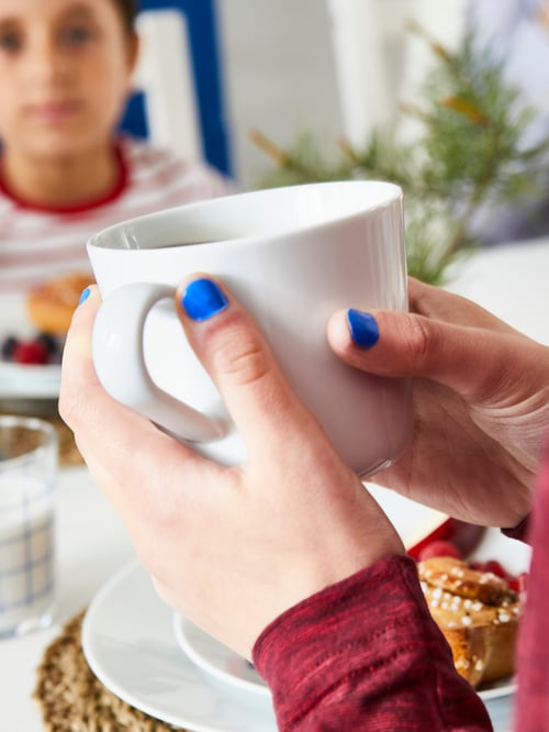 Gros plan sur une chope IKEA 365+ dans les mains d’une femme aux ongles vernis en bleu glacé, avec un petit garçon à l’arrière-plan.