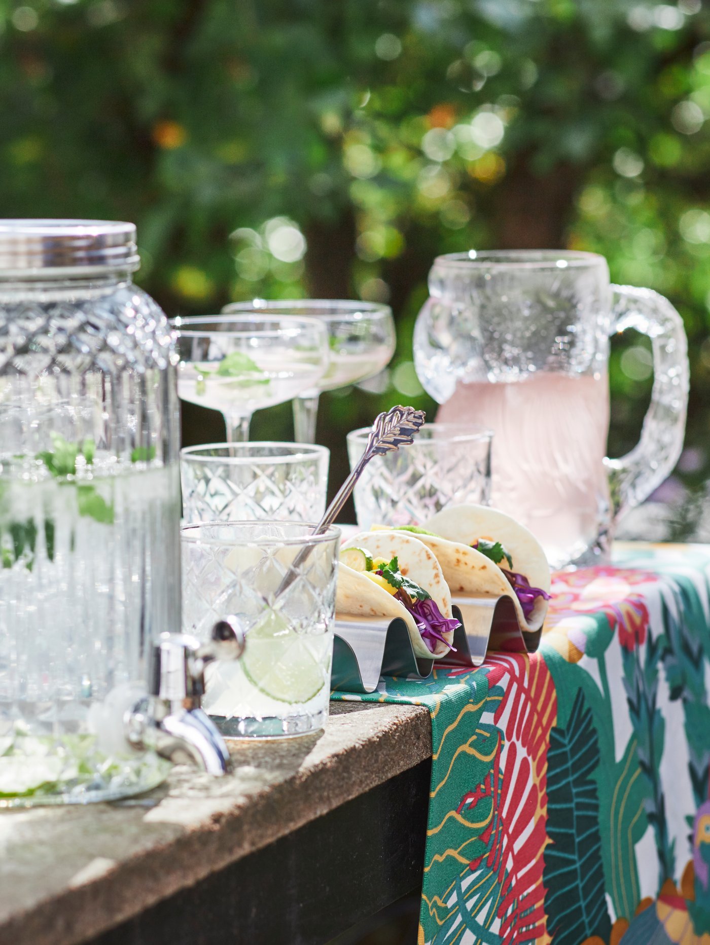 Vanjski stol s poslužavnikom na kojemu su tri plave čaše, a pored njega je ruka koja drži četvrtu.